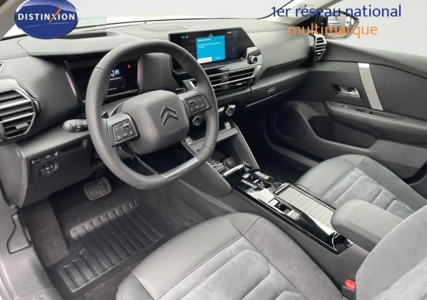 Intérieur de la Citroën C4 2024 vu côté conducteur, avec tableau de bord moderne et sièges gris en cuir et alcantara.