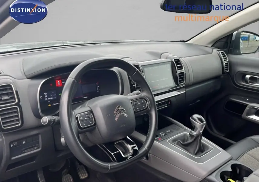 Vue intérieure côté conducteur du Citroën C5 Aircross gris clair, montrant le volant, tableau de bord digital et levier de vitesses manuel.