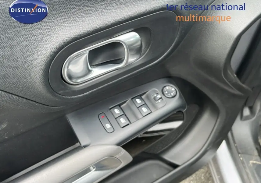 Gros plan sur la porte avant gauche d’un Citroën C5 Aircross gris clair, montrant les commandes des vitres et la poignée intérieure.
