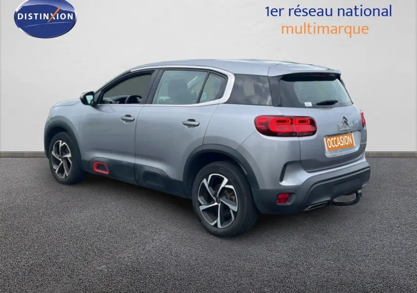 Vue 3/4 arrière droite d'un Citroën C5 Aircross gris clair métal avec jantes alliage et détails rouges sur bas de caisse.