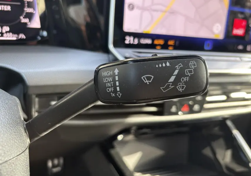 Gros plan sur la commande d’essuie-glace dans l’habitacle de la Volkswagen Golf blanche, avec écran tactile de navigation en arrière-plan.