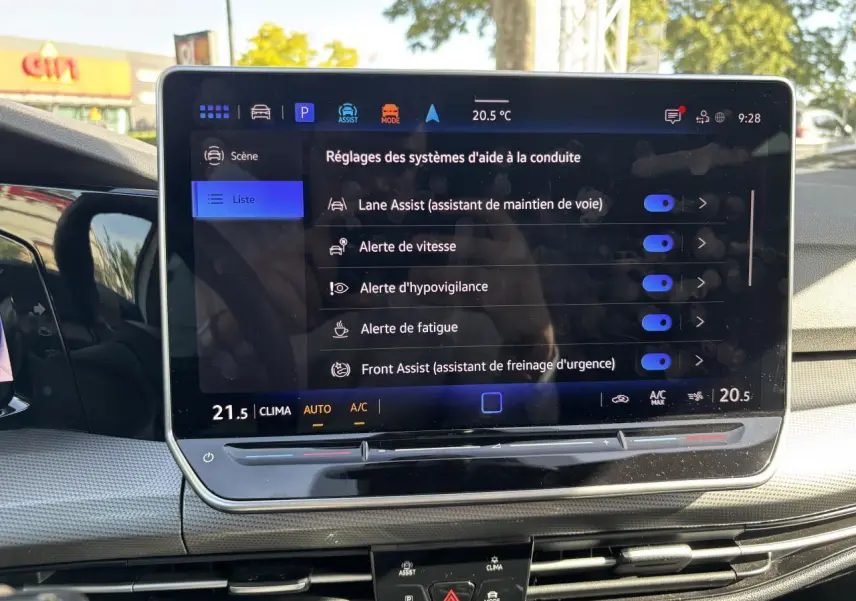 Vue intérieure du tableau de bord de la Volkswagen Golf blanche, écran tactile affichant les aides à la conduite.