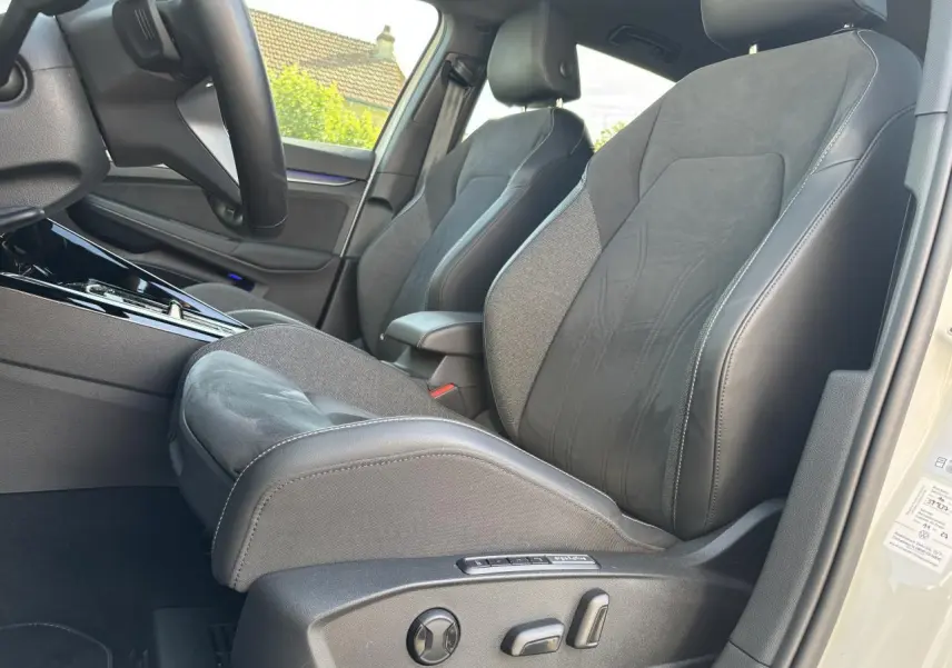 Vue intérieure côté conducteur de la Volkswagen Golf blanche 2024, sièges ergoActive en tissu et cuir avec réglages électriques.