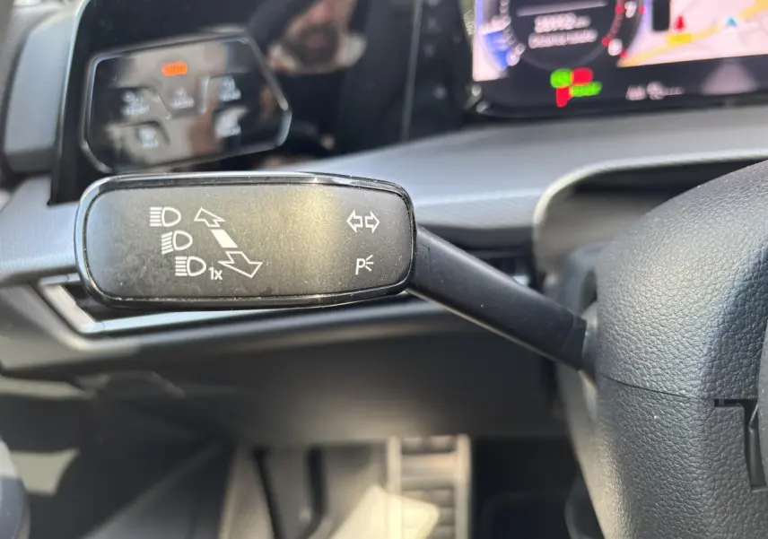 Gros plan sur la commande des feux au volant d’une Volkswagen Golf blanche 2024 avec tableau de bord digital.