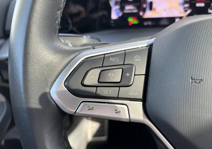Gros plan sur les commandes au volant à gauche de la Volkswagen Golf 1.5 eTSI blanche, avec affichage digital en arrière-plan.