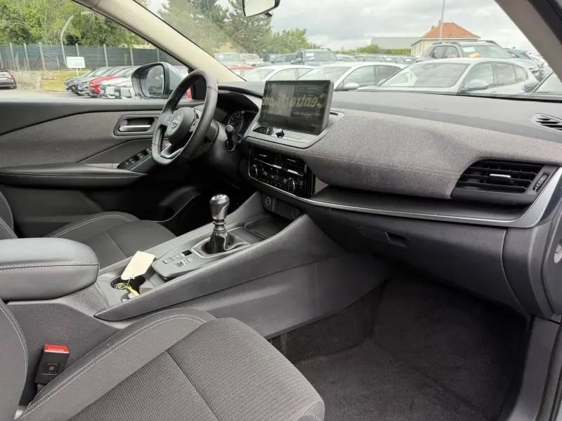 Vue intérieure côté conducteur du Nissan Qashqai 2025 gris Argile, avec tableau de bord moderne et boîte manuelle.