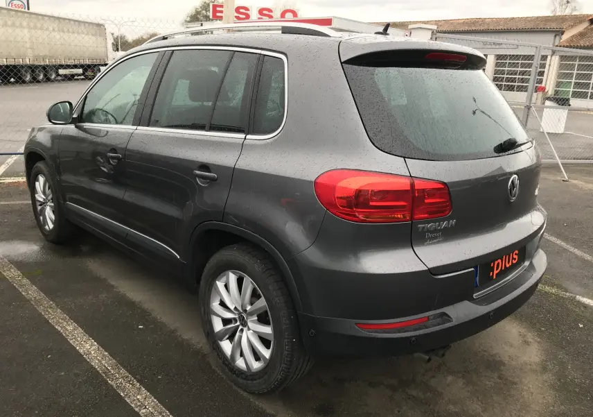 Vue 3/4 arrière gauche d'un Volkswagen Tiguan Sportline gris foncé 2012 avec jantes alliage et feux arrière rouges.
