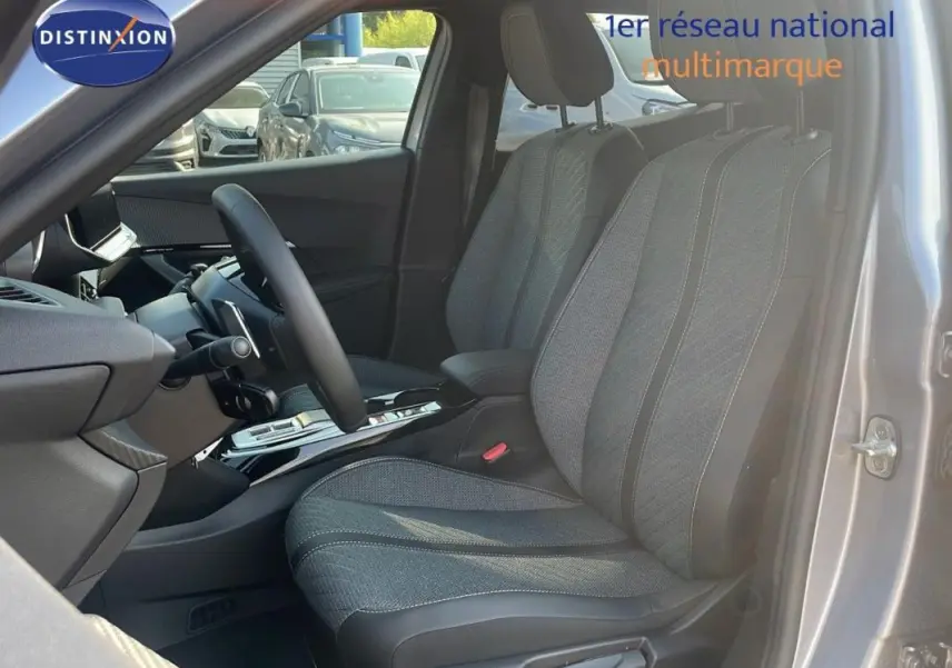 Vue intérieure côté conducteur du Peugeot 2008 gris 2025, montrant les sièges tissu et le volant cuir avec palettes.