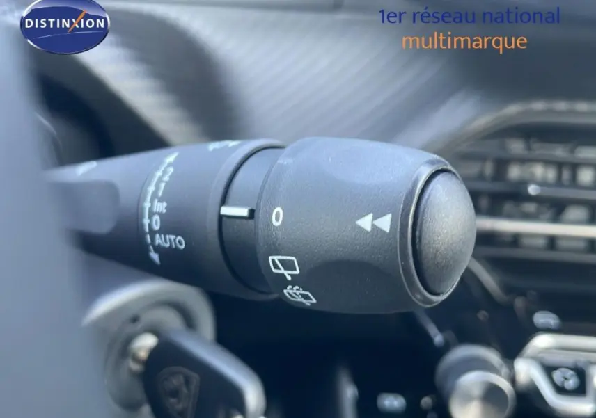 Gros plan sur la commande de l’essuie-glace d’un Peugeot 2008 gris, avec tableau de bord en arrière-plan flou.