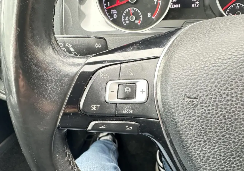 Gros plan sur le volant cuir de la Volkswagen Golf VII gris foncé, avec commandes du régulateur de vitesse et tableau de bord partiel.