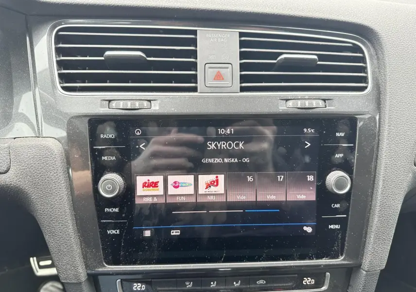 Vue rapprochée de l’écran tactile central du tableau de bord d’une Volkswagen Golf VII gris foncé, affichant la radio Skyrock.