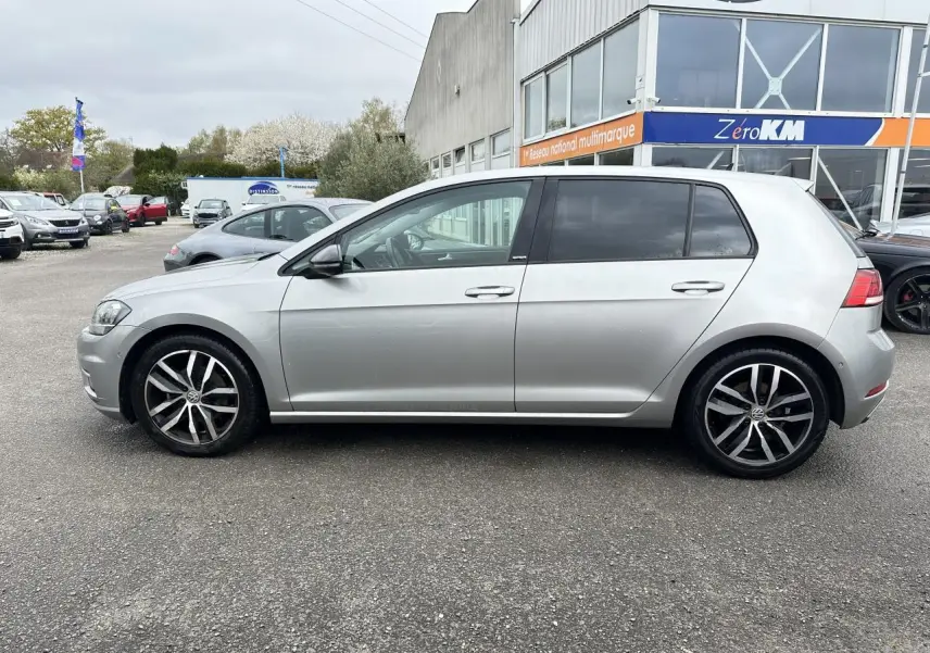 Vue latérale droite d'une Volkswagen Golf VII gris clair avec jantes alliage 17 pouces, vitres arrière surteintées.