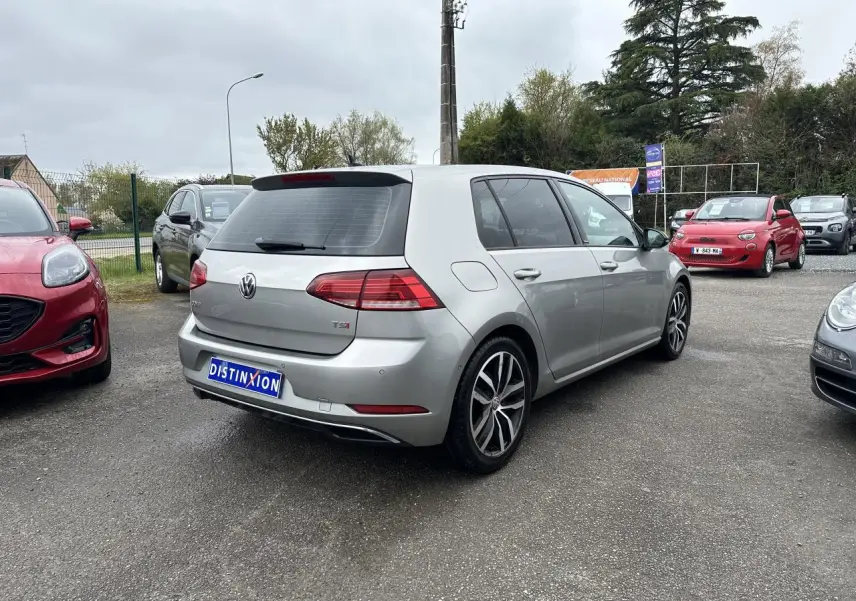 Vue 3/4 arrière droite d'une Volkswagen Golf VII gris clair avec jantes alliage 17 pouces et vitres surteintées.