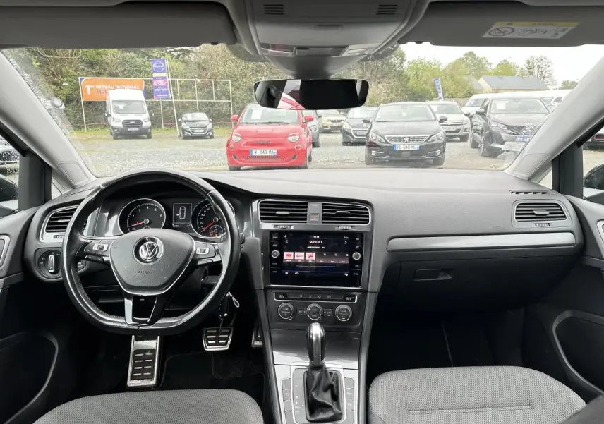 Vue intérieure avant de la Volkswagen Golf VII gris foncé, volant multifonction et écran tactile central allumé.
