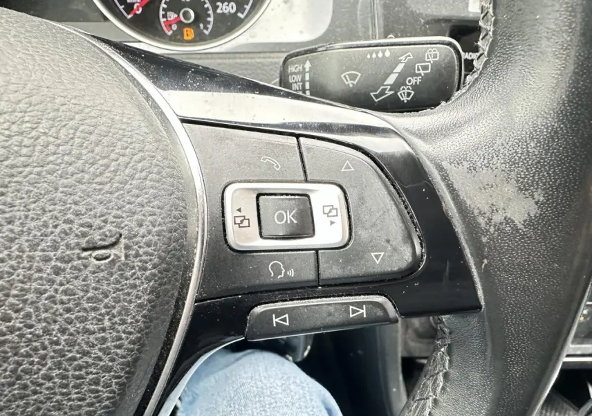 Gros plan sur le volant multifonction en cuir noir de la Volkswagen Golf VII gris foncé, avec commandes intégrées.