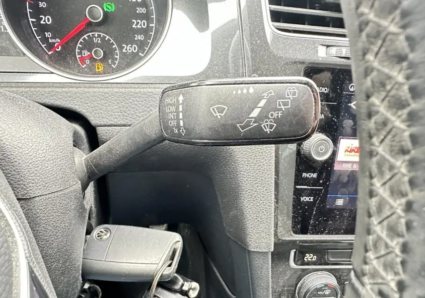 Gros plan sur le commodo d'essuie-glace à gauche du volant d'une Volkswagen Golf VII gris foncé, avec tableau de bord et écran tactile visibles.