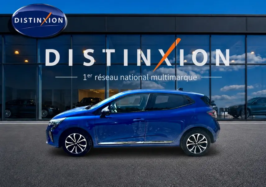 Profil côté gauche d'une Renault Clio V 1.0 TCe 90 Techno bleu iron avec jantes alu devant une vitrine Distinxion.