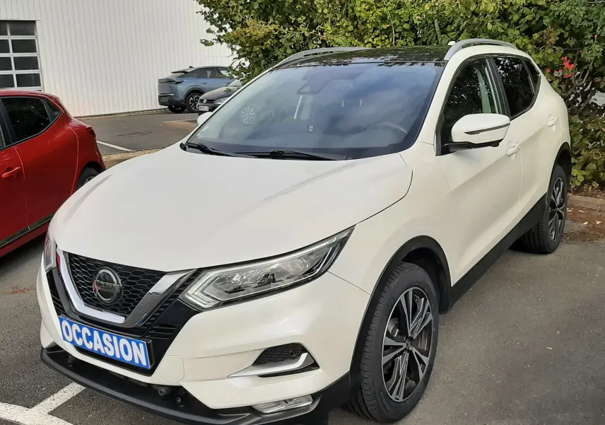 Nissan Qashqai blanc vue 3/4 avant droit, toit noir, jantes alliage bicolores, stationné en extérieur.