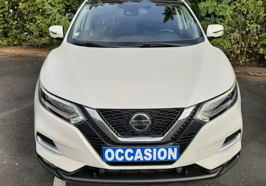 Vue avant d'un Nissan Qashqai blanc 2018 avec calandre noire et plaque "OCCASION" sur un parking.