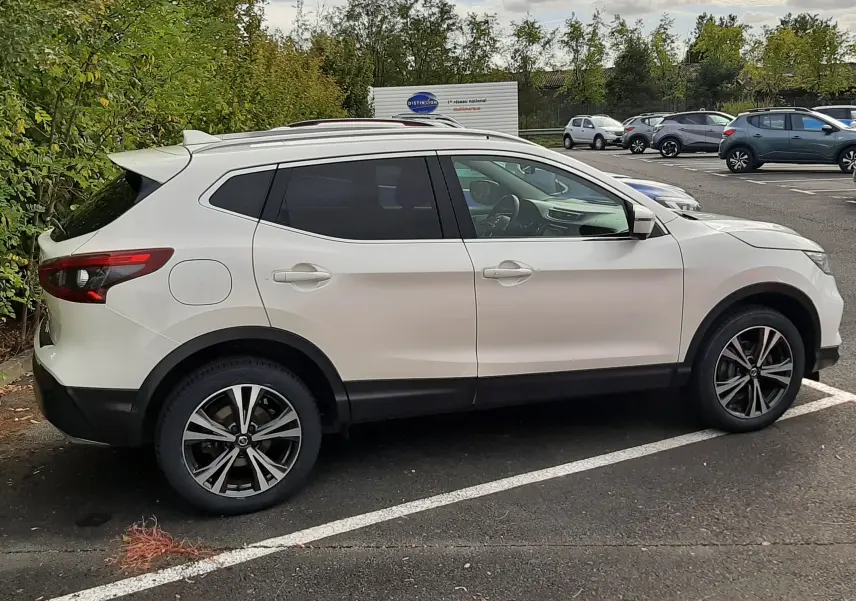 Vue de profil côté droit d'un Nissan Qashqai blanc 2018 avec jantes alliage bicolores sur un parking extérieur.