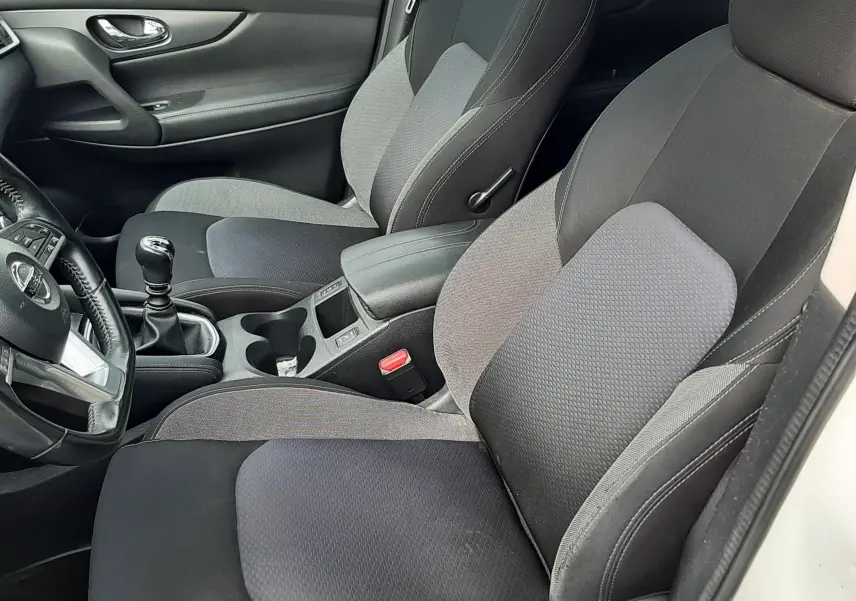 Vue intérieure côté conducteur du Nissan Qashqai blanc 2018, sièges tissu gris et noir avec levier de vitesse manuel visible.