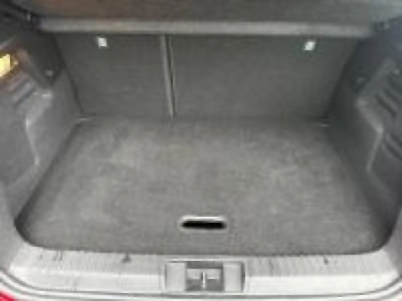 Coffre spacieux et vide du Renault Captur rouge, vue plongeante montrant le tapis et les parois intérieures noires.