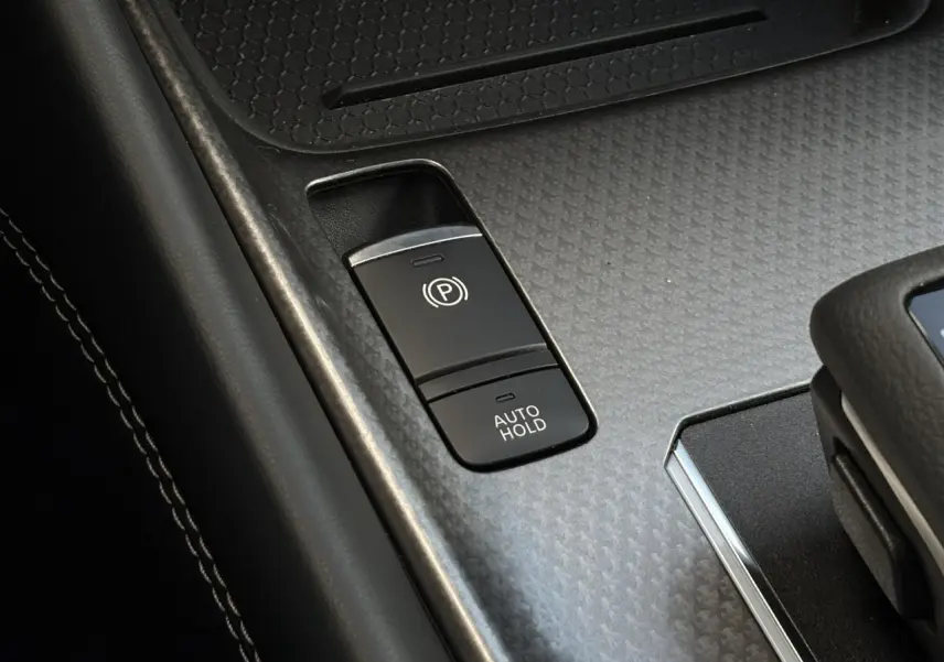 Gros plan sur la console centrale du Nissan Qashqai 2025, montrant les boutons du frein à main électrique et Auto Hold.