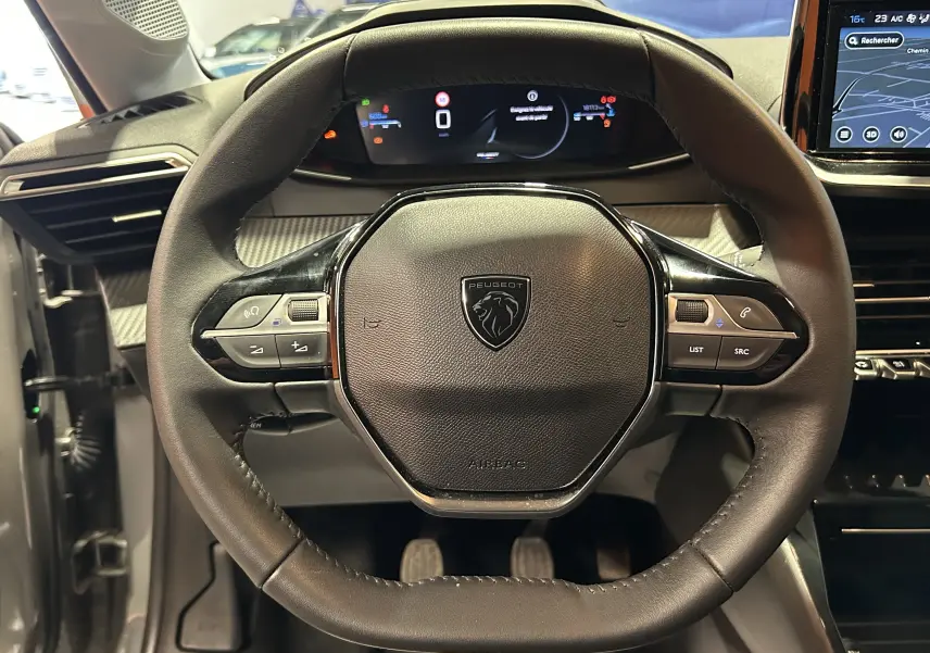 Vue rapprochée du volant cuir noir de la Peugeot 208 2025 avec tableau de bord digital et écran GPS visible à droite.