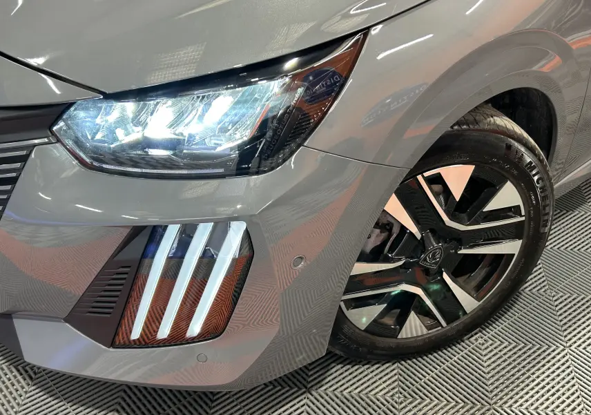 Gros plan sur l'avant droit gris Selenium de la Peugeot 208 2025, mettant en valeur le phare LED et la jante alliage noire et argent.
