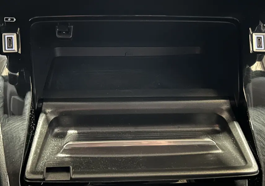 Détail du compartiment de rangement central avant de la Peugeot 208 Turbo 100 BVM6 Allure, finition noire brillante.