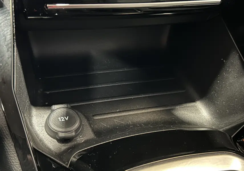 Prise 12V en gros plan dans la console centrale noire de la Peugeot 208 Turbo 100 BVM6 Allure gris Selenium.