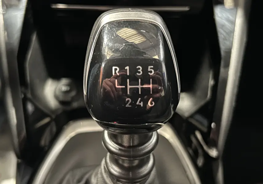Gros plan sur le levier de vitesses manuel noir de la Peugeot 208 Turbo 100, montrant la grille des 6 rapports et la marche arrière.