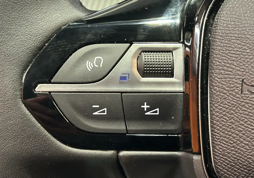 Gros plan sur les commandes de volume au volant d'une Peugeot 208 gris Selenium, boutons noirs avec symbole audio.