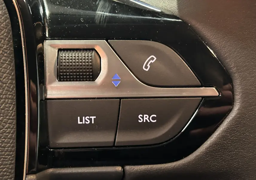 Gros plan sur les commandes au volant noir brillant de la Peugeot 208 Turbo 100 BVM6 Allure, boutons LIST, SRC et téléphone.