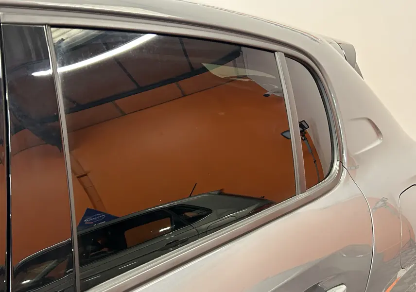 Détail du côté arrière droit gris Selenium d'une Peugeot 208 Turbo 100 BVM6 Allure avec vitre teintée et poignée de porte visible.