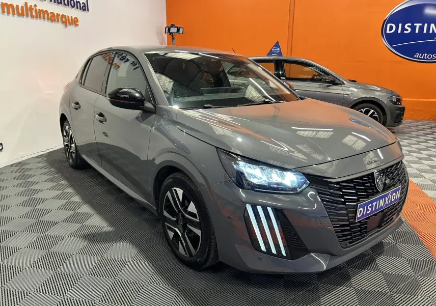 Peugeot 208 gris Selenium vue 3/4 avant droit avec phares LED allumés en intérieur showroom.