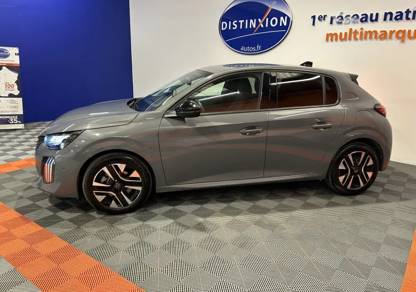 Peugeot 208 gris Selenium vue de profil côté gauche, avec jantes alliage et feux avant allumés en intérieur showroom.