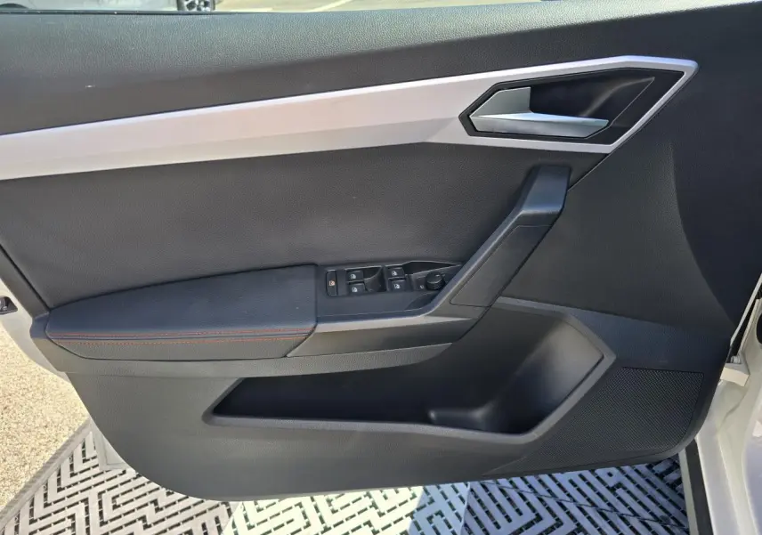 Vue intérieure de la porte avant gauche d'une SEAT Arona blanche, avec garniture noire et surpiqûres rouges.