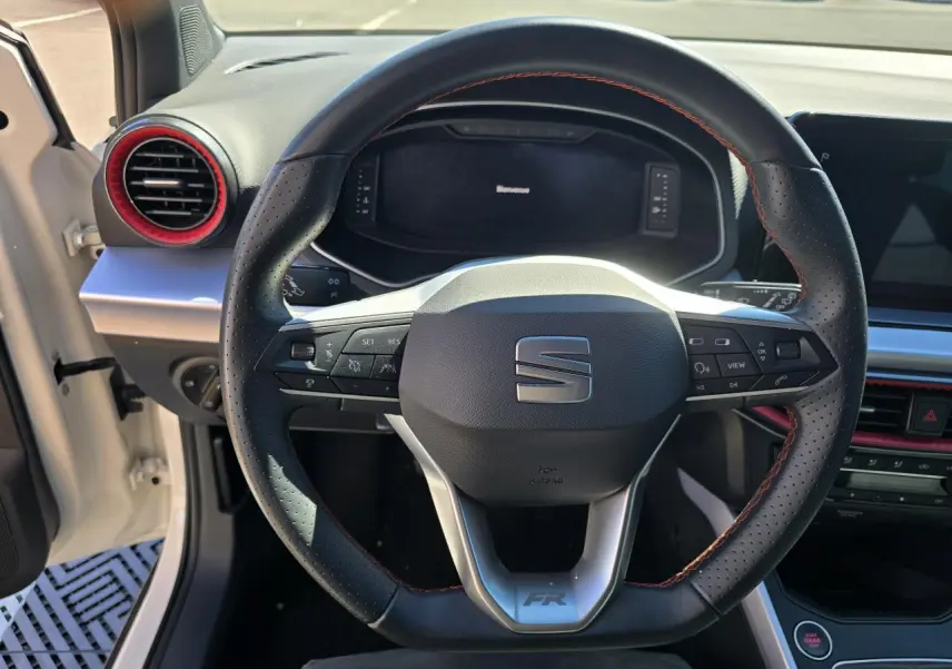 Vue rapprochée du volant sport en cuir noir avec surpiqûres rouges du SEAT Arona blanc toit noir, tableau de bord et aérateurs rouges visibles.