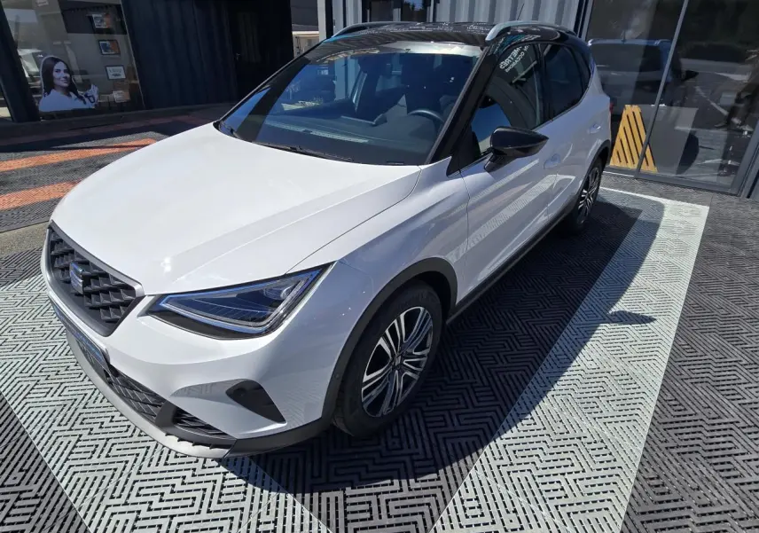 Vue 3/4 avant droite d'une SEAT Arona 2024 blanche avec toit noir et jantes alliage distinctives.