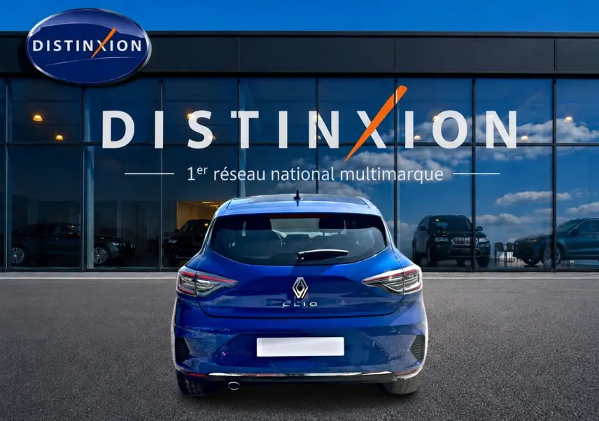 Vue arrière d'une Renault Clio V bleu iron garée devant une vitrine avec logo Distinxion visible.