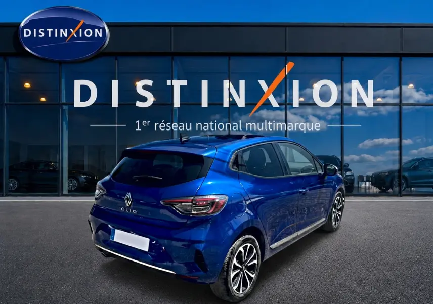 Renault Clio V bleu iron vue 3/4 arrière droit, avec jantes alu et becquet arrière visible devant vitrine Distinxion.