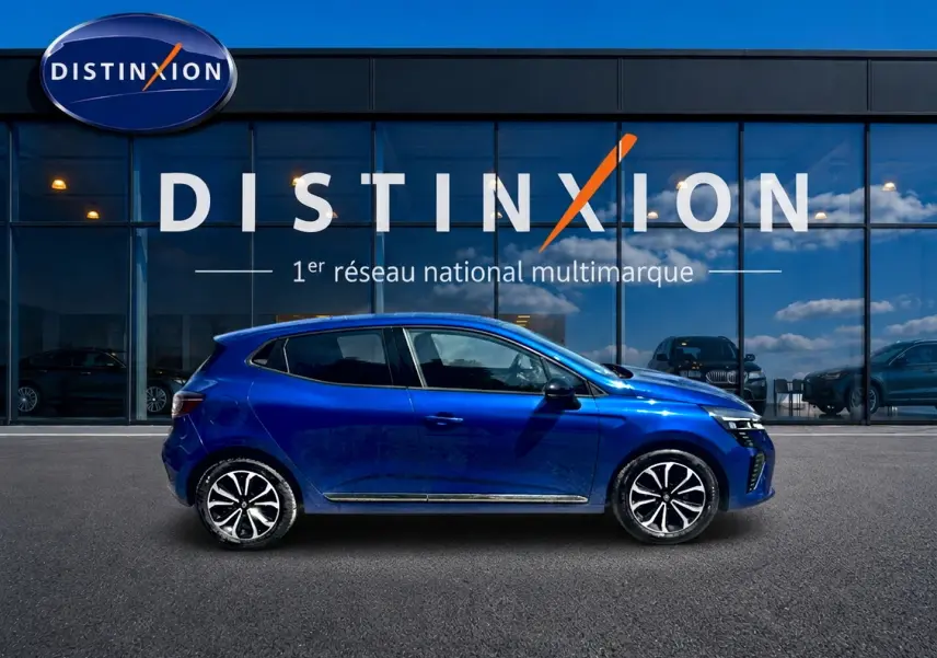 Profil droit d'une Renault Clio V bleu iron 2025 avec jantes alliage et poignées ton carrosserie devant un showroom Distinxion.