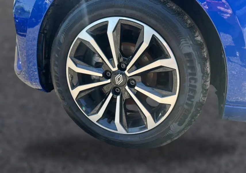 Gros plan sur la roue avant gauche avec jante alu bicolore et partie de la carrosserie bleu iron de la Renault Clio V.