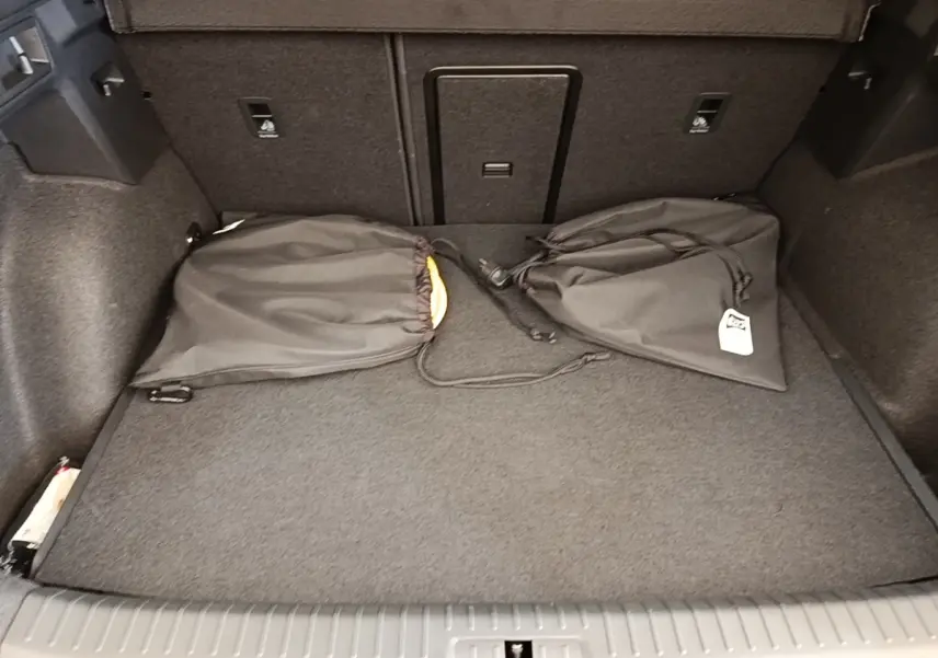 Vue intérieure du coffre du CUPRA Formentor 1.4 e-HYBRID 2024 avec tapis gris et deux sacs noirs posés.