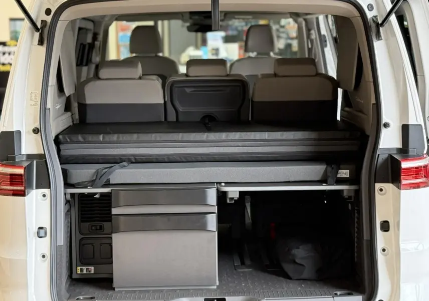 Vue arrière ouverte du Volkswagen California T7 blanc Candy, montrant la banquette et la mini-cuisine intégrée.