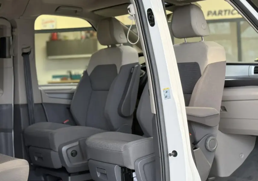 Vue intérieure côté droit du Volkswagen California T7 blanc Candy, montrant les sièges avant avec accoudoirs et appuis-tête.