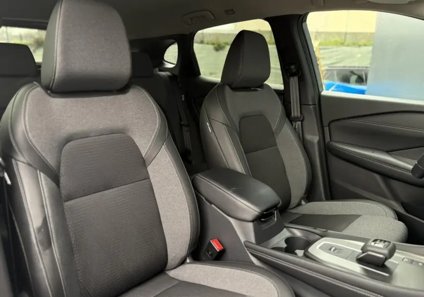 Vue intérieure des sièges avant gris clair et noir du Nissan Qashqai 2024, avec accoudoir central et console moderne.