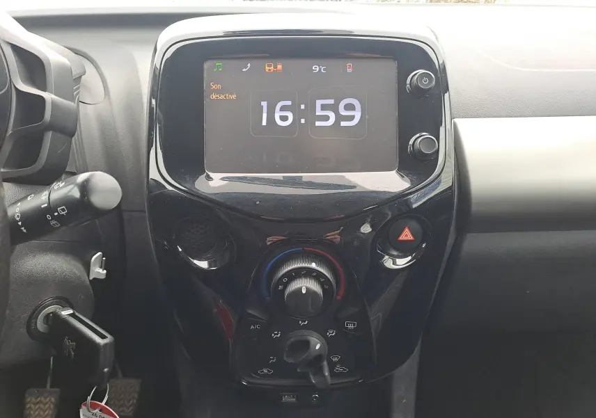 Vue rapprochée du tableau de bord central noir brillant de la Peugeot 108 2016 avec écran digital et commandes climatisation.