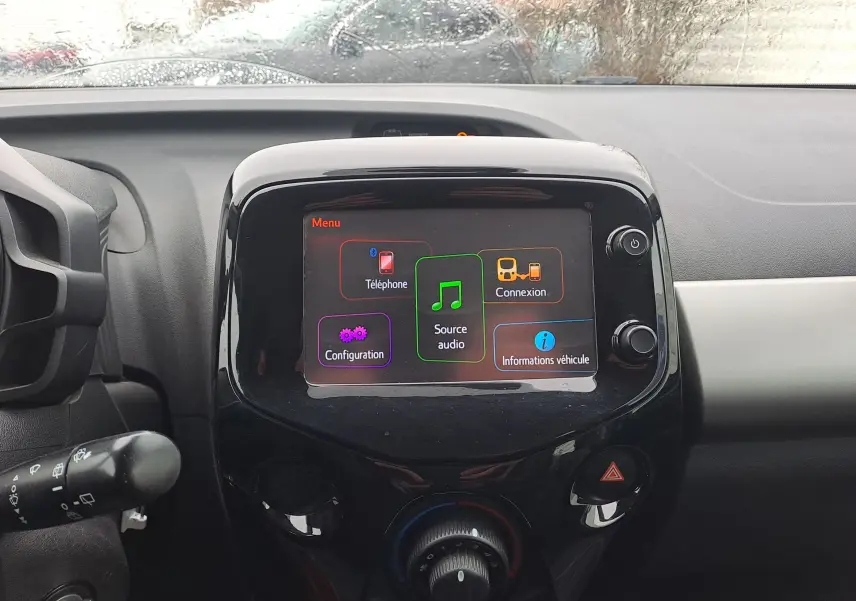 Vue rapprochée de l’écran tactile central noir brillant du tableau de bord d’une Peugeot 108 bleu, affichant le menu multimédia.